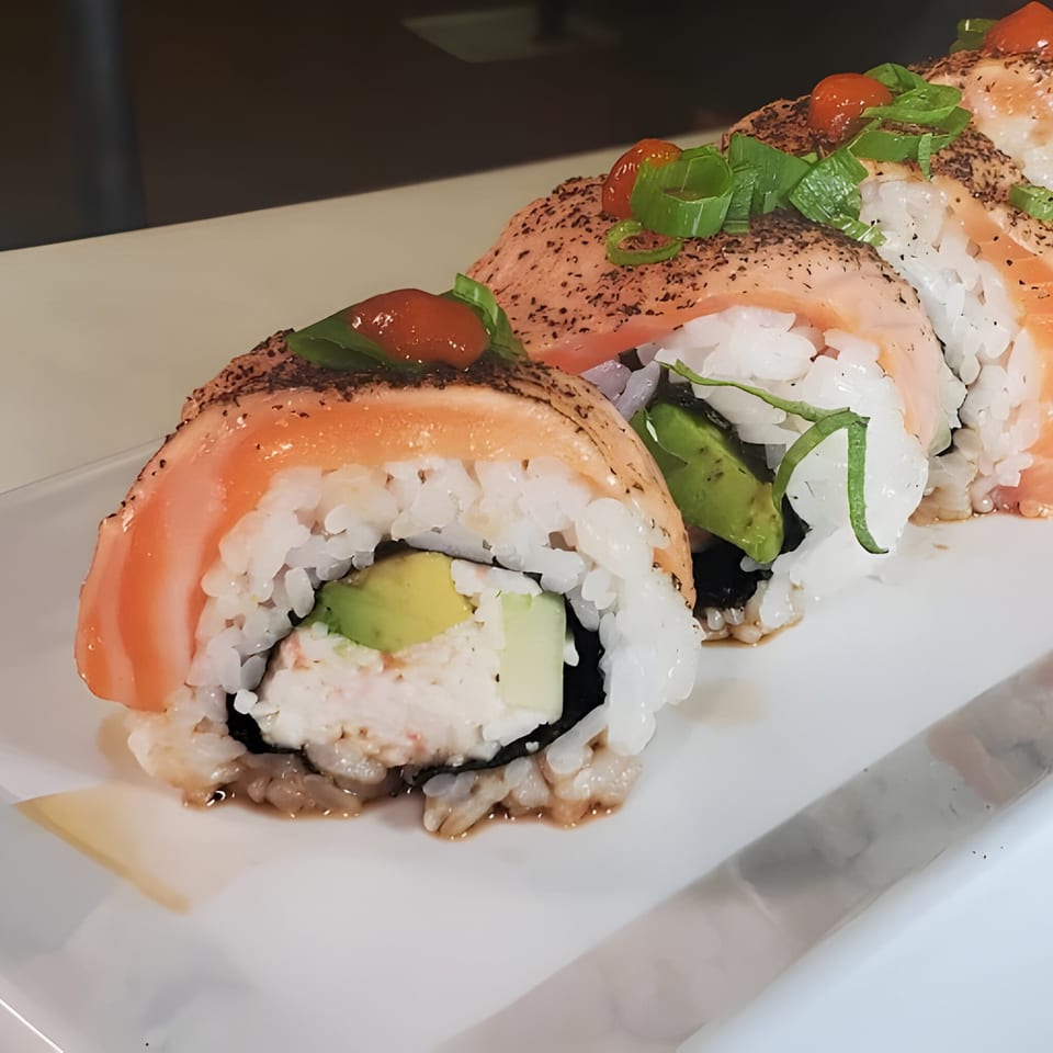 Four salmon sushi rolls with avocado, cream cheese, and green onions on a white plate.