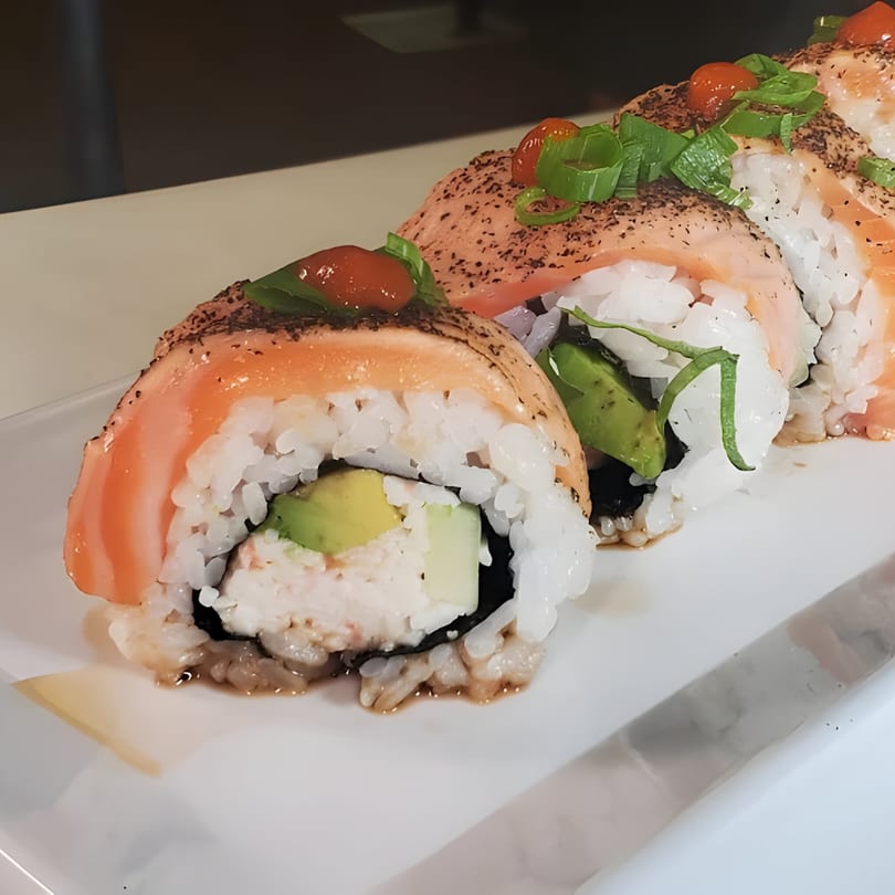 Four salmon sushi rolls with avocado, cream cheese, and green onions on a white plate.