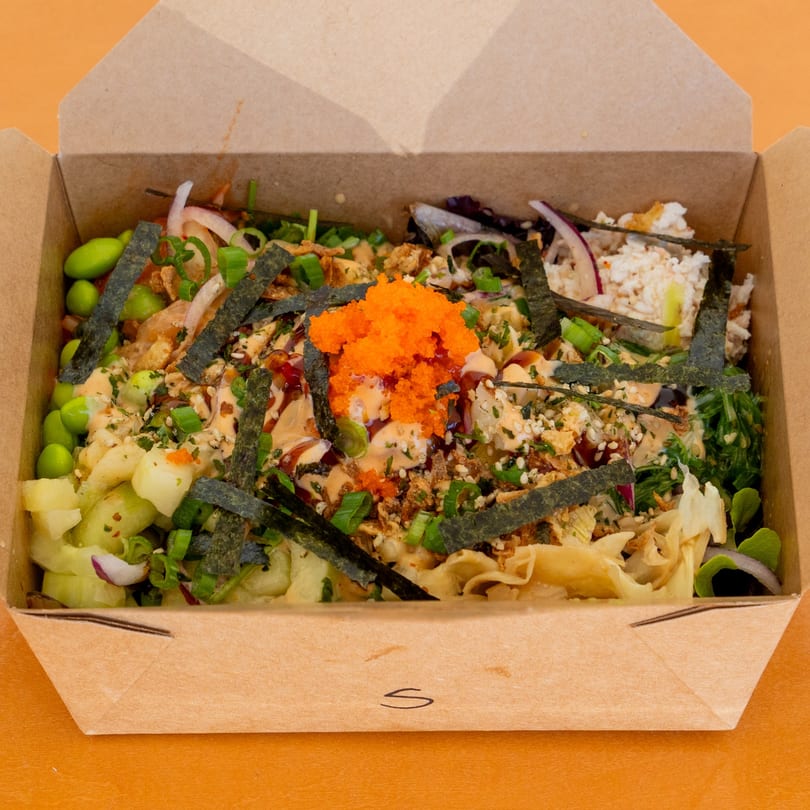 Jimmy's Poke bowl in a cardboard takeout container, topped with roe, seaweed, and sauce.