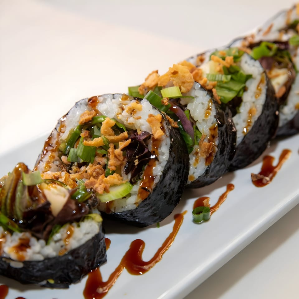 Sliced sushi burrito with rice, seaweed, green onions, crispy toppings, and sauce on a white plate.