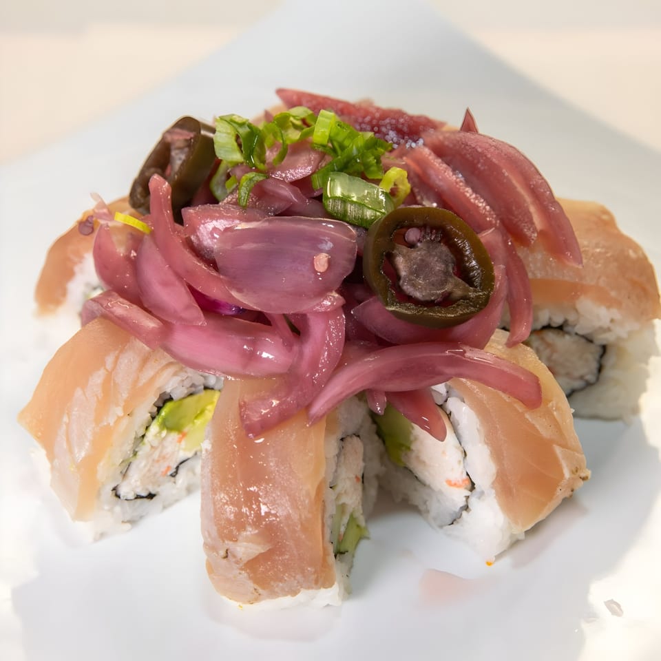 Sushi rolls topped with pickled red onions, sliced jalapeños, and green onions on a white plate.