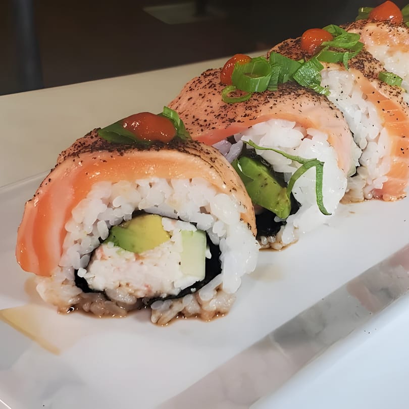 Close-up of a sushi burrito with salmon, avocado, and green onions on a white plate.