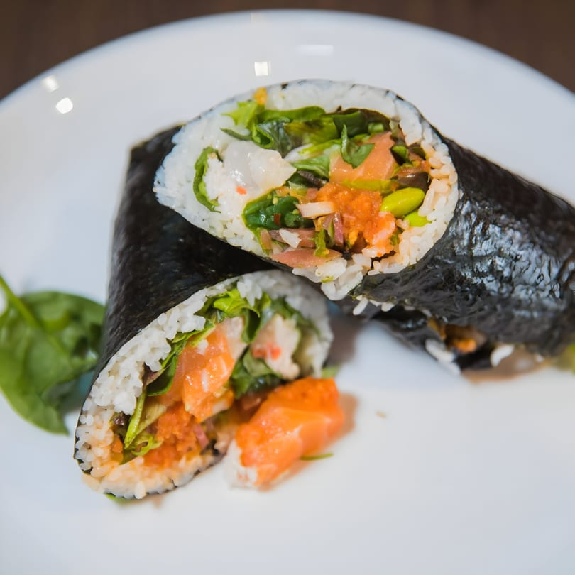 Two halves of a Jimmy's Poke & Sushi Burrito, filled with salmon, rice, and greens.